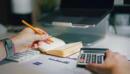 Freelancer pracuje u notebooku na faktury do zahraničí s papíry, poznámkami a kalkulačkou